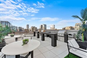 Terraço no telhado com mobiliário de exterior, churrasqueira e plantas em vasos.