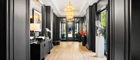 A hallway with a wooden floor, a chandelier, a bust sculpture, and a desk with a lamp.
