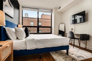 Quarto de hotel moderno com uma cama grande, uma escrivaninha, uma cadeira e televisão na parede.