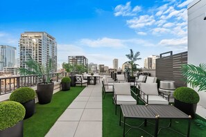 Terraço no telhado com área de estar externa, plantas em vasos e vista para a cidade.