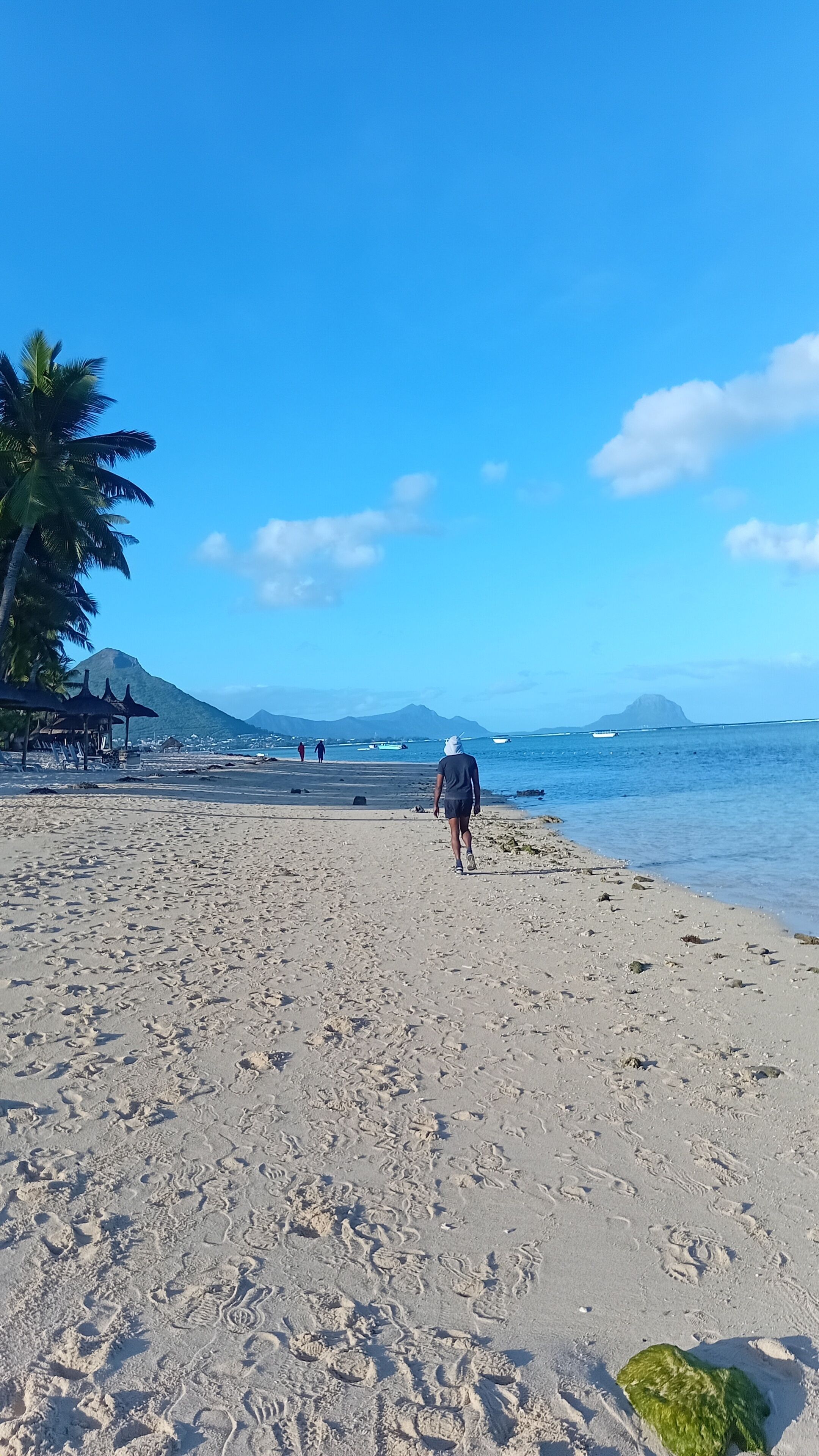A beach with footprints, a person walking, and a mountain in the background.