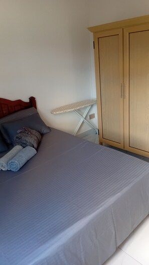Ein Schlafzimmer mit einem Bett, Kissen, einem Holzschrank und einem weißen Bügelbrett.