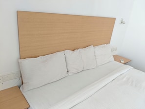 A bed with a wooden headboard, white bedding, and a bedside table with a phone.