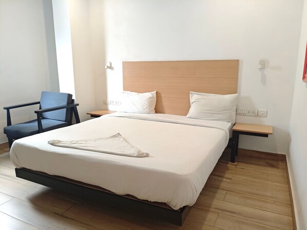 Una cama bien hecha con cabecera de madera, una mesita de noche y una silla.