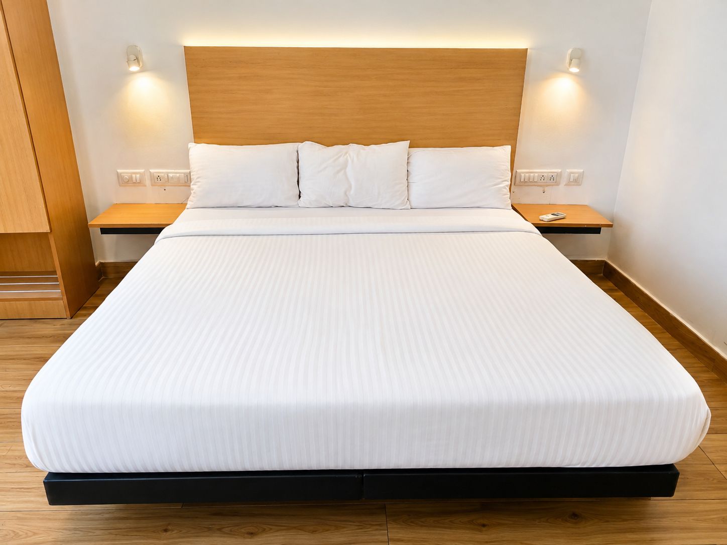 A neatly made bed with a wooden headboard, two bedside tables, and wall-mounted lights.
