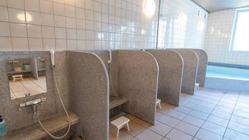 A modern bathroom with multiple shower cubicles, a small sink area, and a tiled floor.