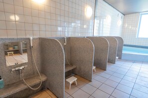 Un baño moderno con varios cabina de ducha, un pequeño espacio con lavamanos y suelo de baldosas.