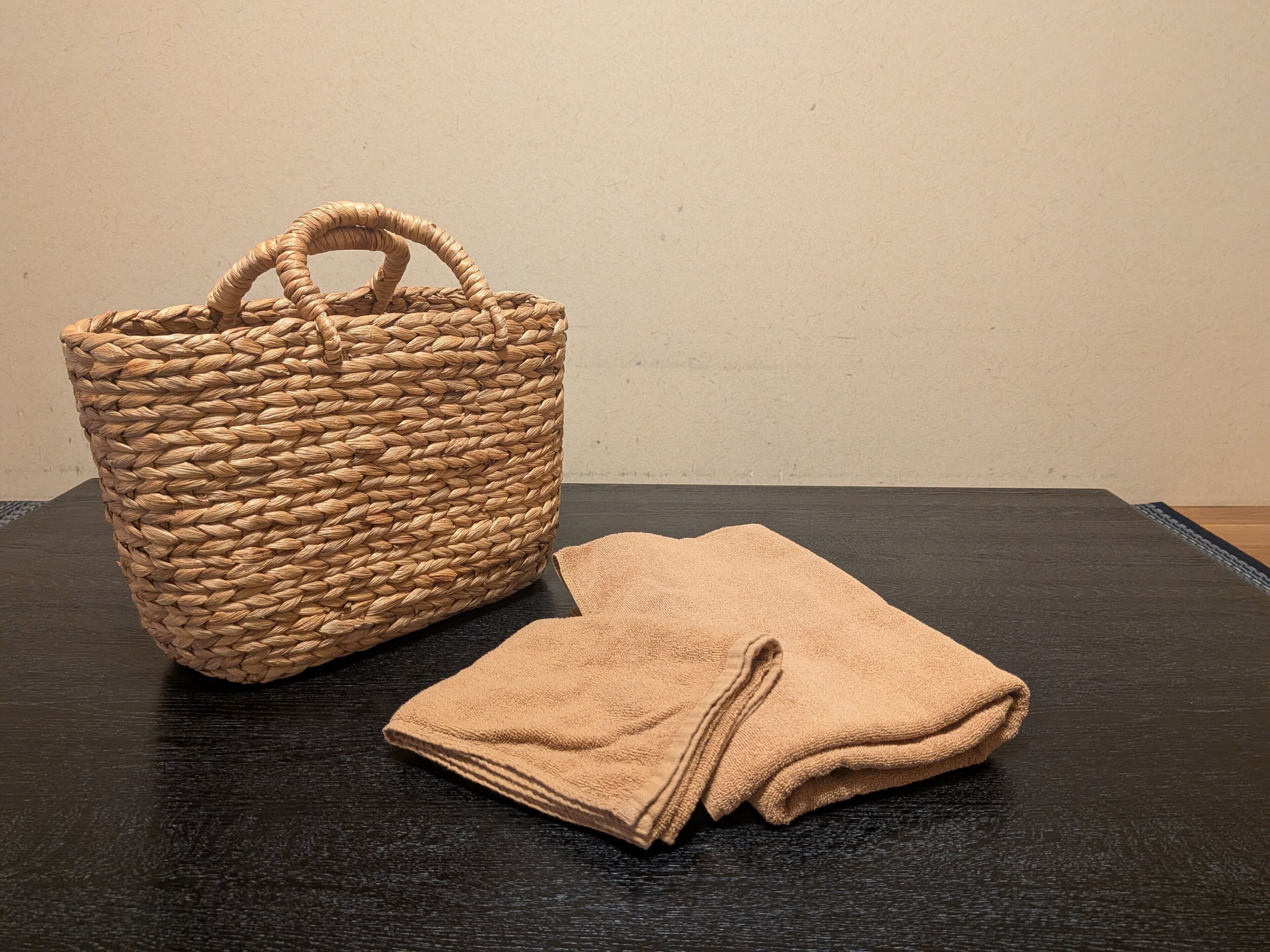 Een gevlochten mand en opgevouwen handdoeken op een donker oppervlak, voor een effen muur.
