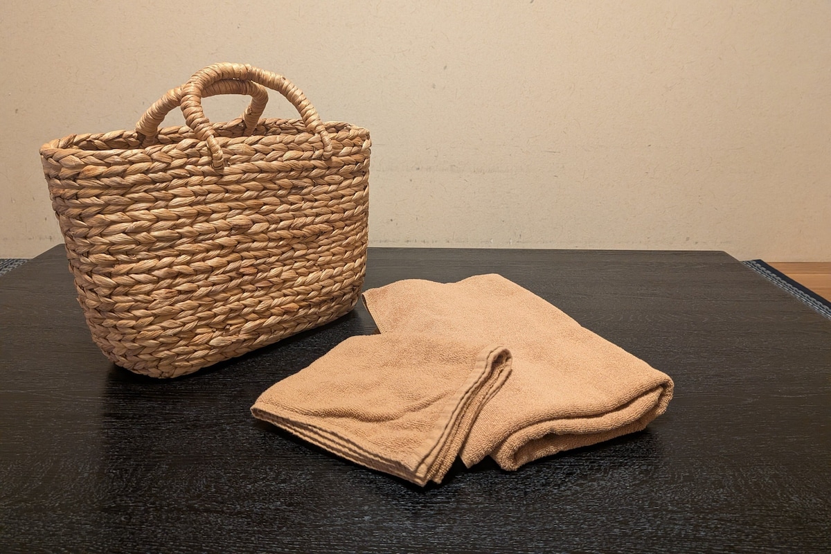 A woven basket and folded towels on a dark surface against a plain wall.