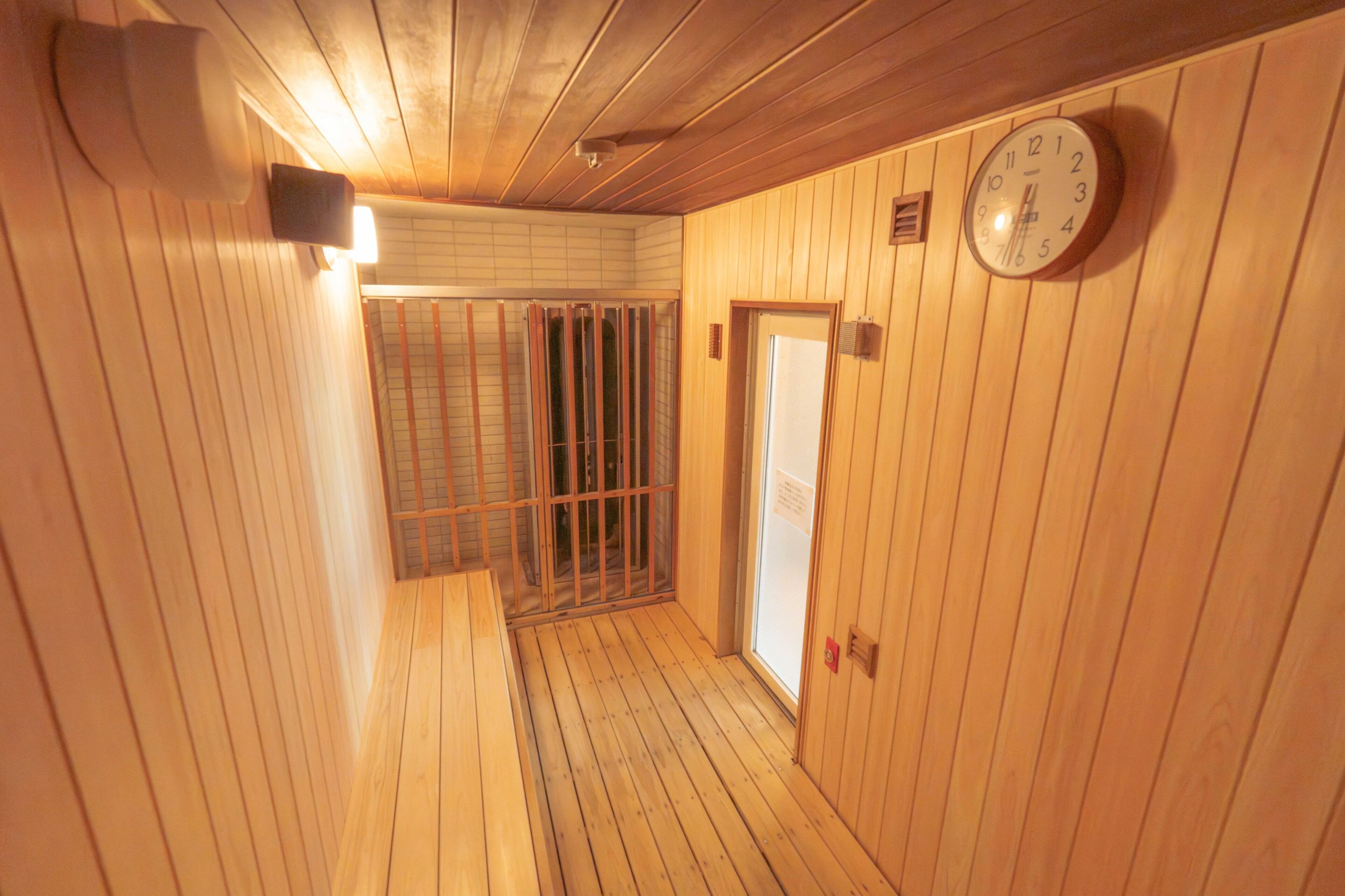 A wooden interior hallway with a clock on the wall, a door, and a barred window.