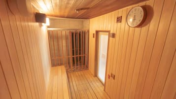 A wooden interior hallway with a clock on the wall, a door, and a barred window.