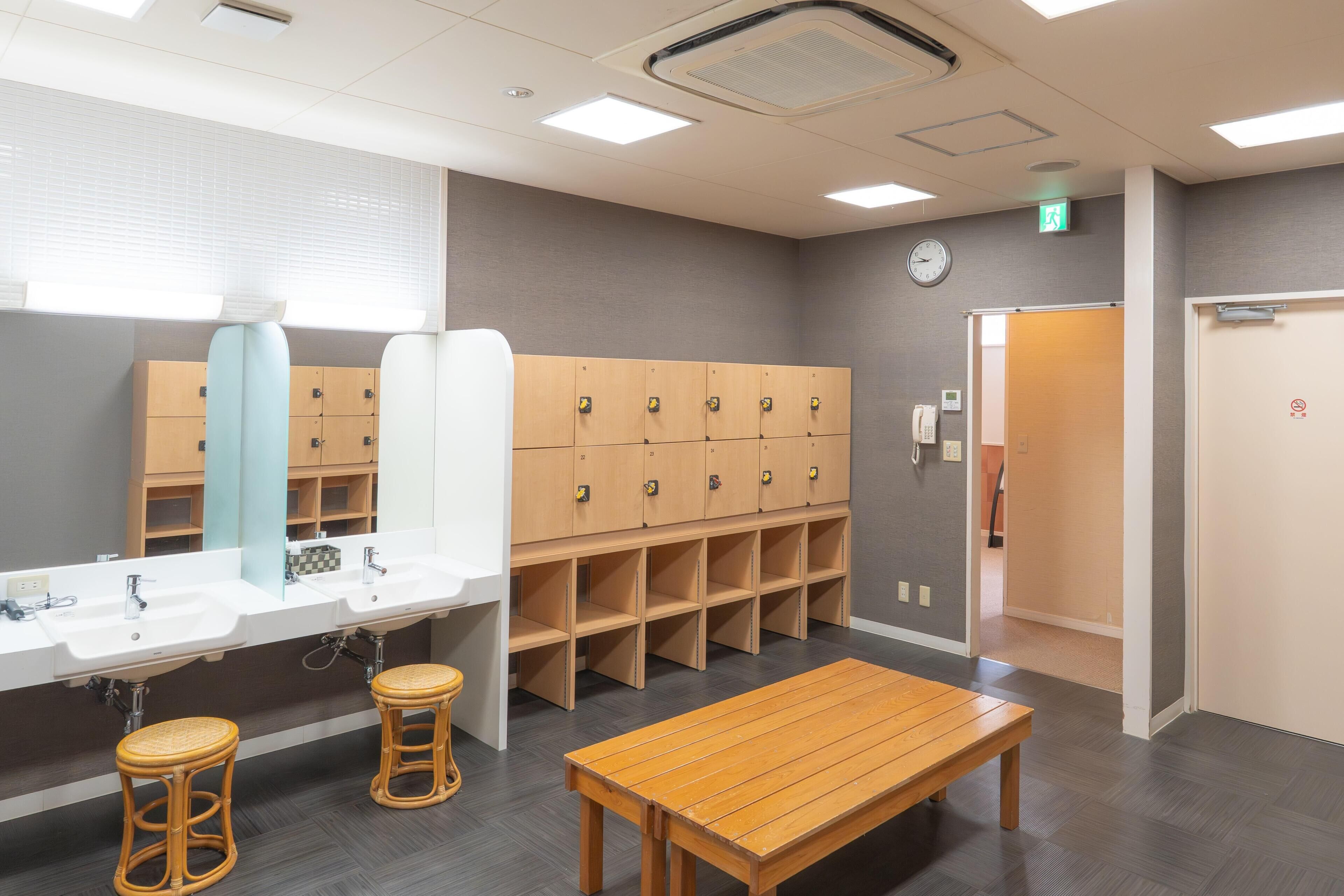 A hotel bathroom with a large mirror, multiple lockers, a wooden bench, and a sink.