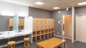 A hotel bathroom with a large mirror, multiple lockers, a wooden bench, and a sink.
