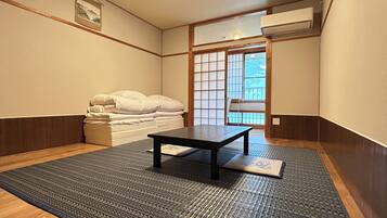 A traditional Japanese room with tatami flooring, a low table, a futon bed, and a sliding door leading to a balcony.