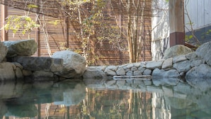 Un área de piscina al aire libre tranquila con agua cristalina, rodeada de rocas y paredes de bambú.