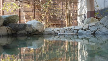 A tranquil outdoor pool area with clear water, surrounded by rocks and bamboo walls.
