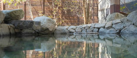 Un área de piscina al aire libre tranquila con agua cristalina, rodeada de rocas y paredes de bambú.