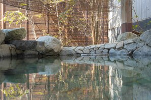 A tranquil outdoor pool area with clear water, surrounded by rocks and bamboo walls.