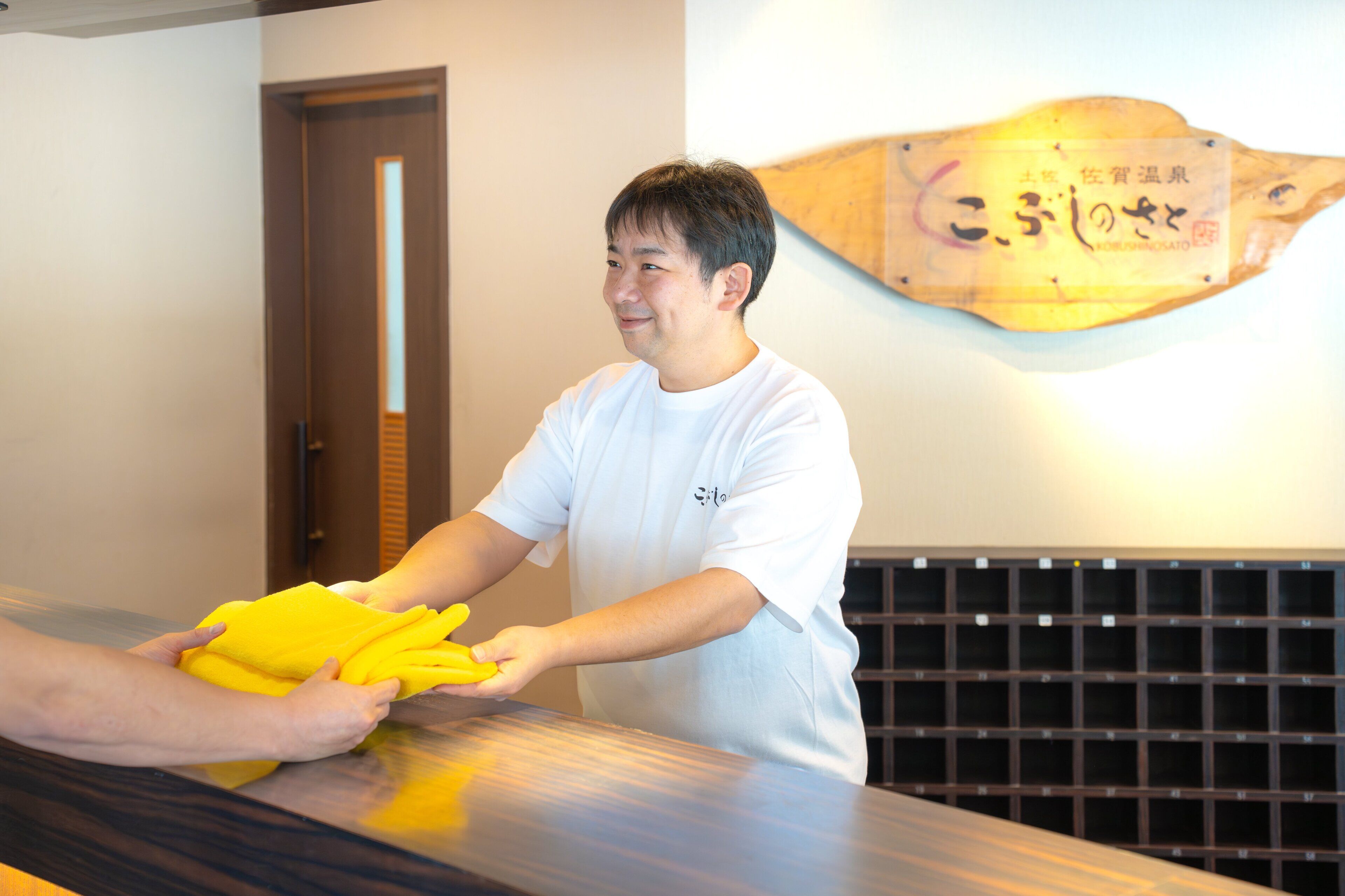 A person handing over a yellow item to another person at a counter with a wooden plaque on the wall.