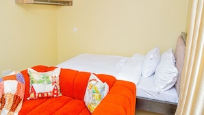 Ein Bett mit weißer Bettwäsche, ein rotes Sofa mit gemusterten Kissen und ein Holzschrank über dem Bett.