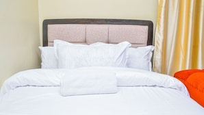 Ein Bett mit weißer Bettwäsche und Kissen, ein gefaltetes weißes Handtuch und ein orangefarbener Sessel.