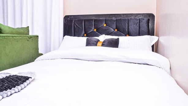 Ein Bett mit einem gepolsterten Kopfteil, weißer Bettwäsche und einem grünen Kissen.