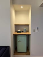 Una kitchenette compacta con un refrigerador pequeño, una encimera de madera y una lámpara.