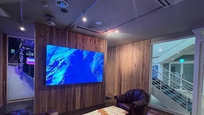 Habitación con una gran televisión de pantalla plana montada en una pared de madera, sillones de cuero, una mesa de centro de mármol y una puerta de cristal que da a una escalera.