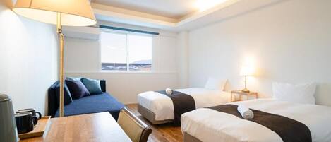 A hotel room with two beds, a desk, a lamp, and a view of the outdoors.
