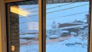 Una ventana con vistas a un paisaje nevado, que incluye un edificio y un coche estacionado.