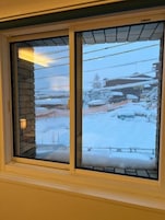 Una ventana con vistas a un paisaje nevado, que incluye un edificio y un coche estacionado.