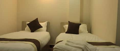 A hotel room with two single beds, each with a pillow and a blanket.