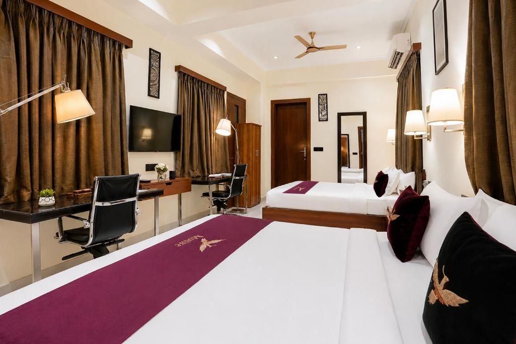 A hotel room with a desk, two beds, a television, and a ceiling fan.