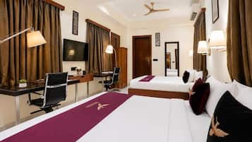 A hotel room with a desk, two beds, a television, and a ceiling fan.