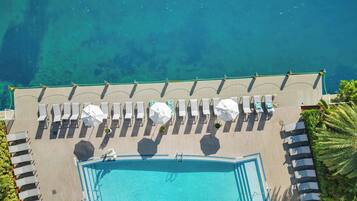 Ein Luftbild eines Resorts mit Schwimmbad, Liegestühlen und Strand.