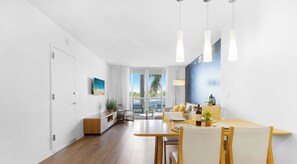 A modern living room with a dining area, large windows, and a view of the outdoors. - 2BR • Marina Views at Beachwalk (Hallandale Beach)