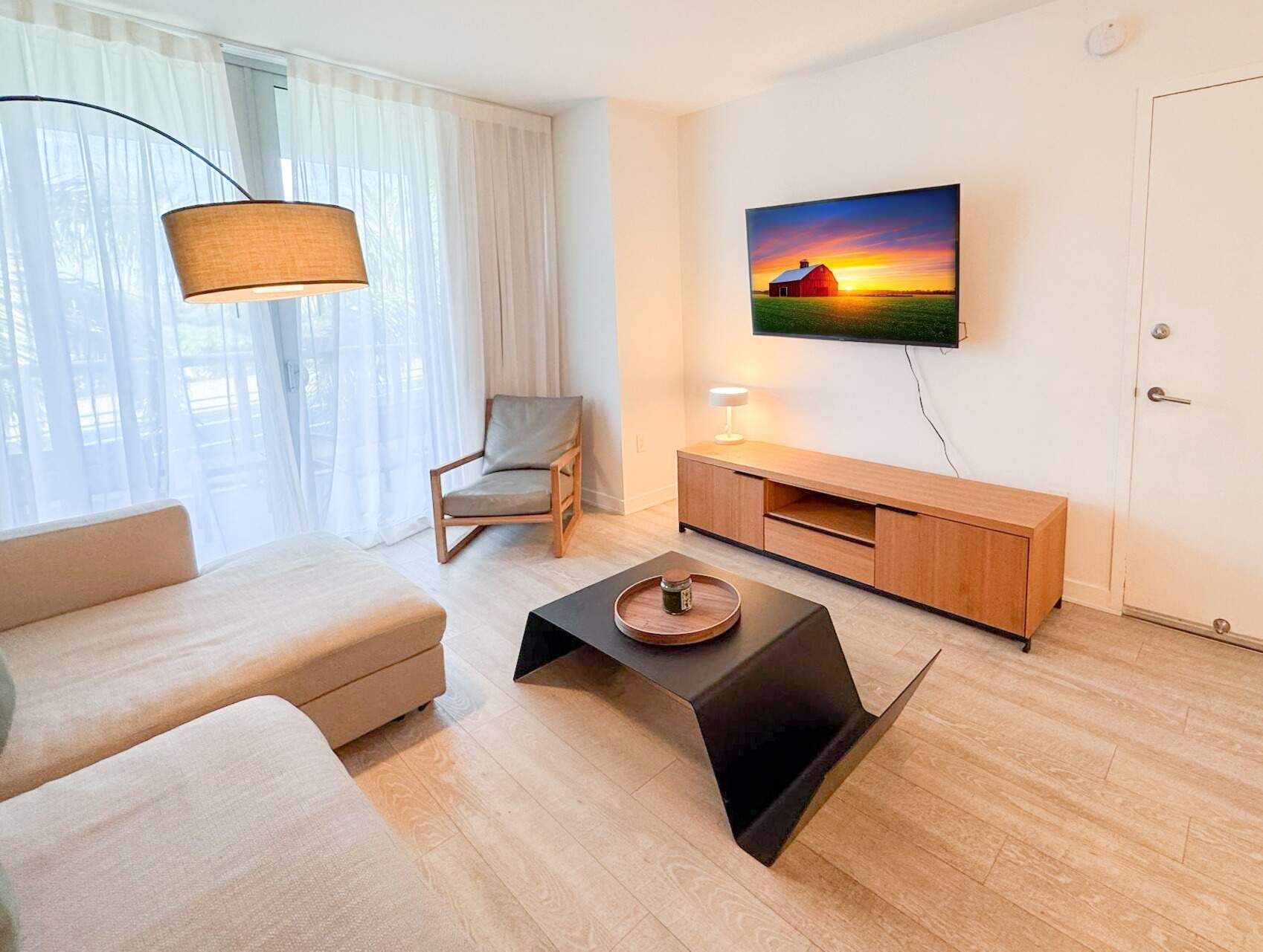 A modern living room with a sofa, a chair, a coffee table, a TV mounted on the wall, and a wooden cabinet.