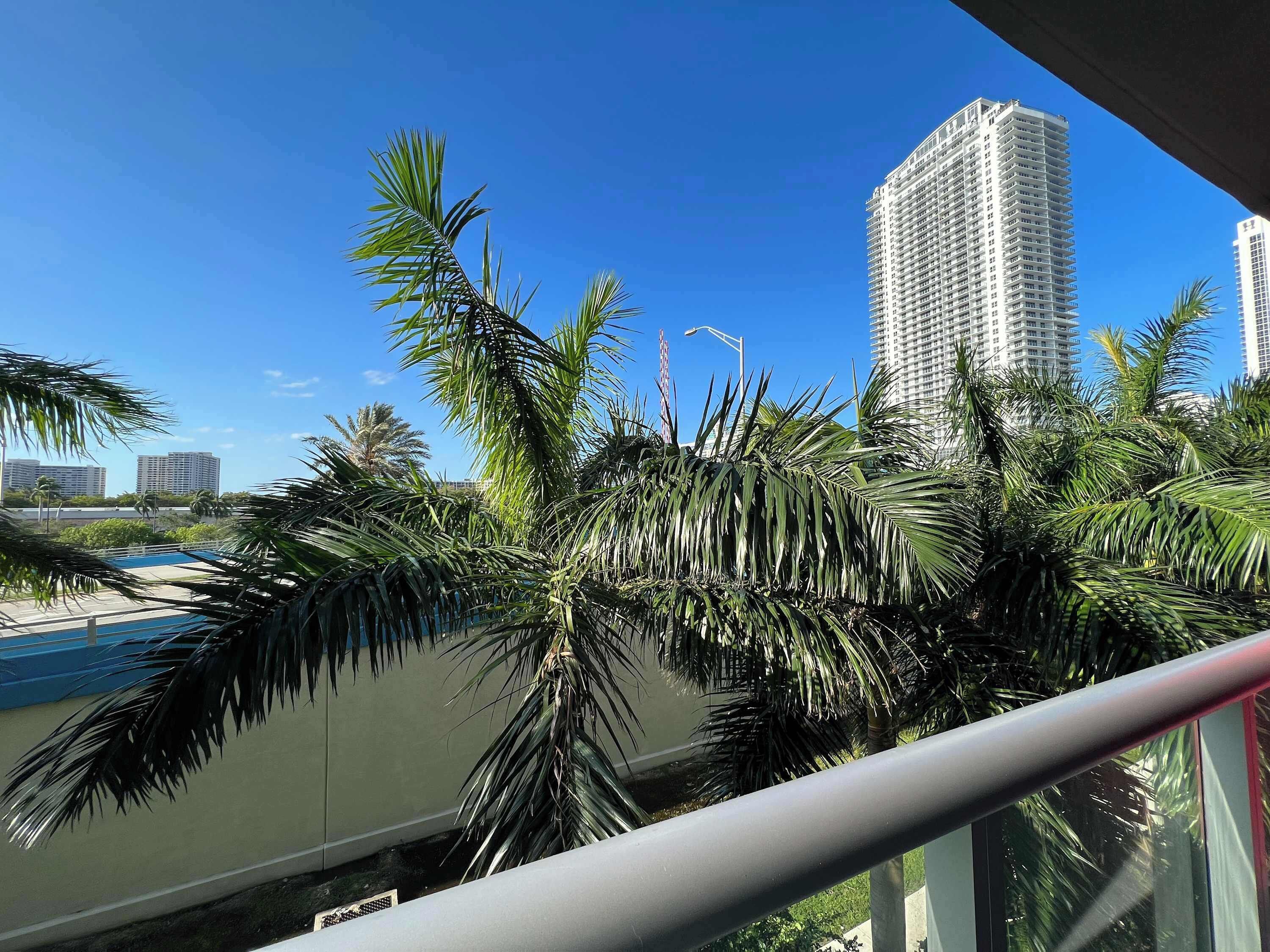 A balcony with a view of tall buildings and palm trees.