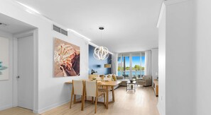 A modern living room with a dining area, large windows, and a view of a pool. - 2BR Resort Living | Pool + Gym (Hallandale Beach)