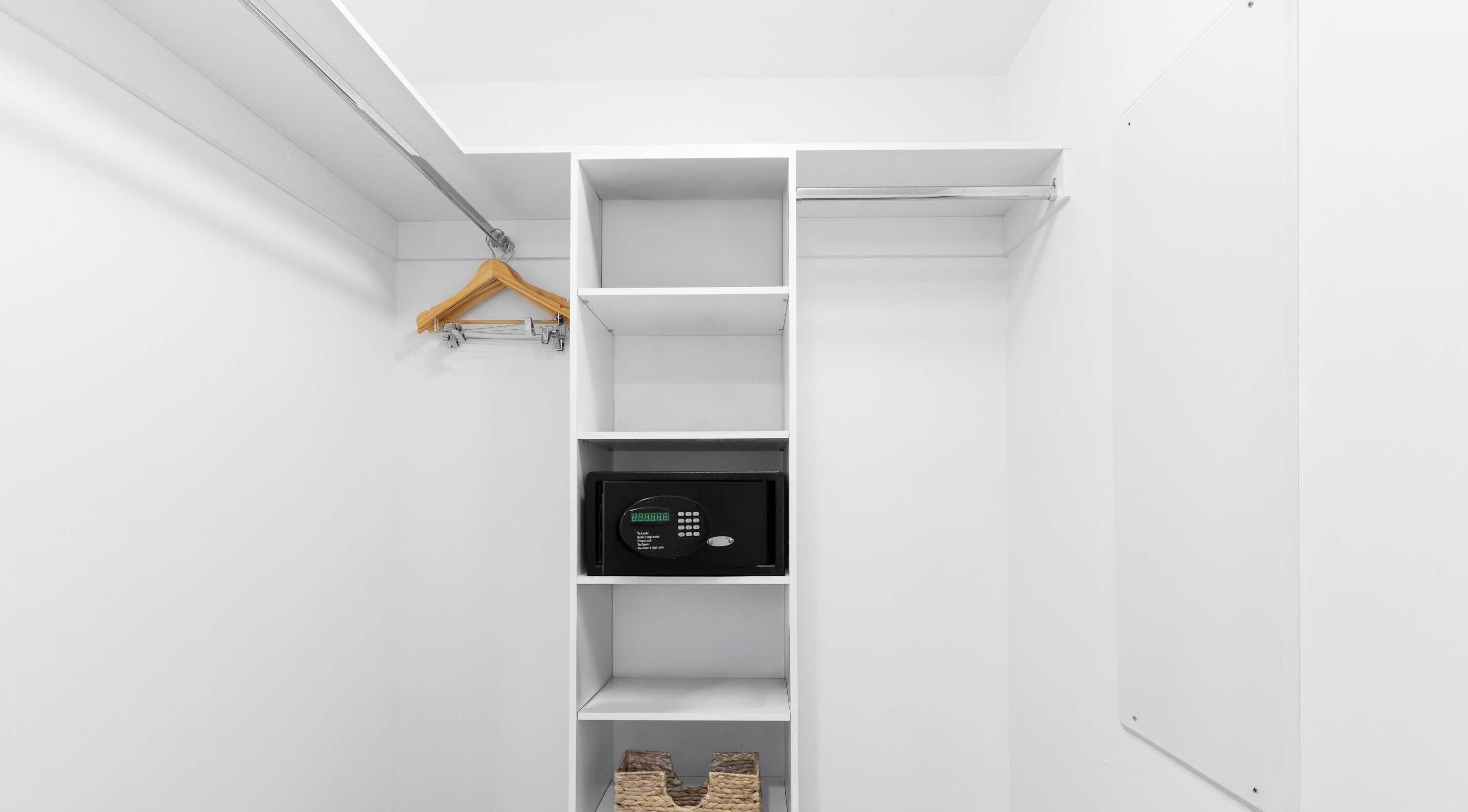 Um armário branco com uma barra para pendurar roupas, um cofre preto e duas cestas de vime.