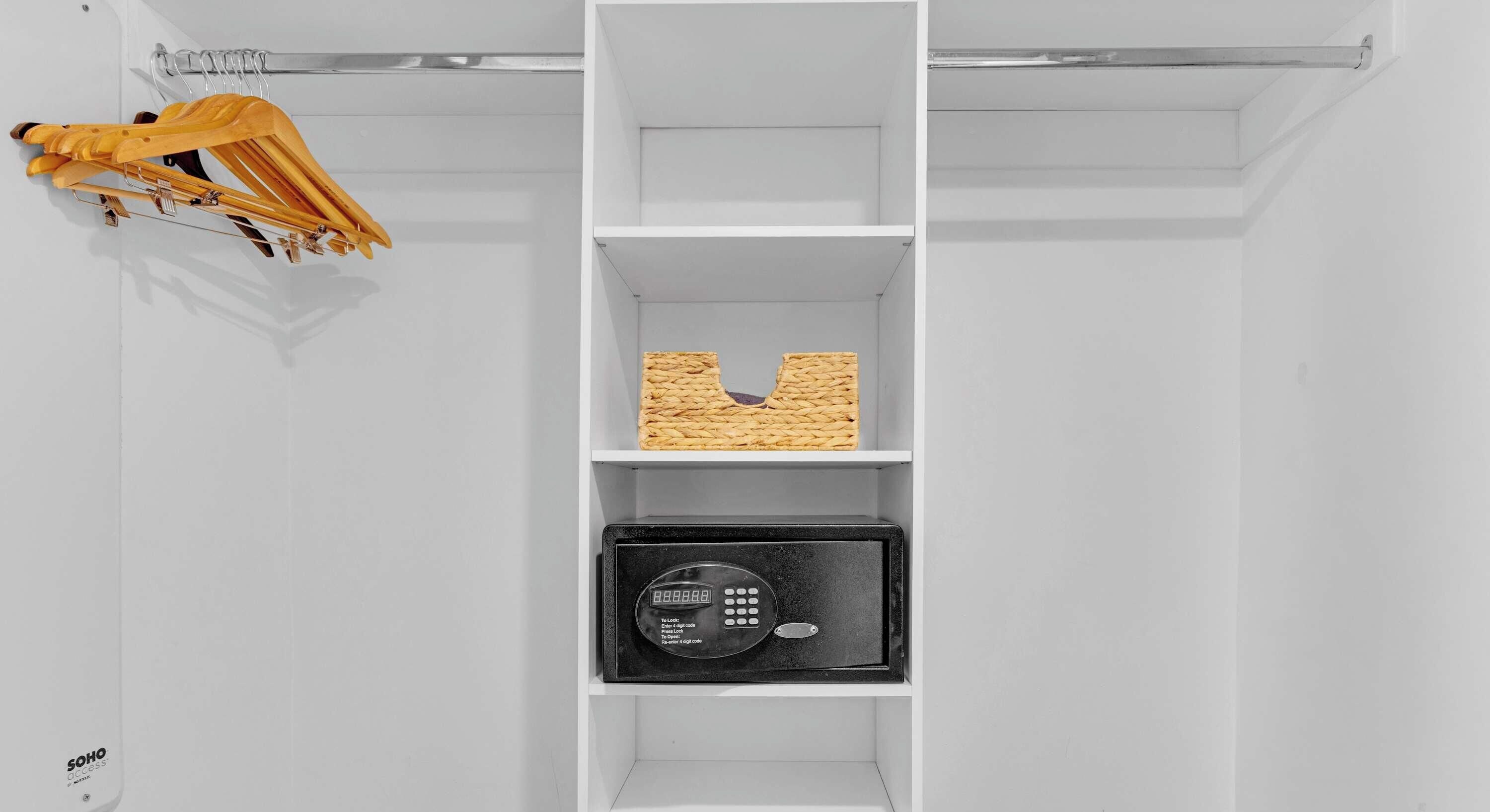 Een witte kast met een kledingroede aan de linkerkant, een gevlochten mand op het middelste plankje, en een zwart elektronisch apparaat onderin.