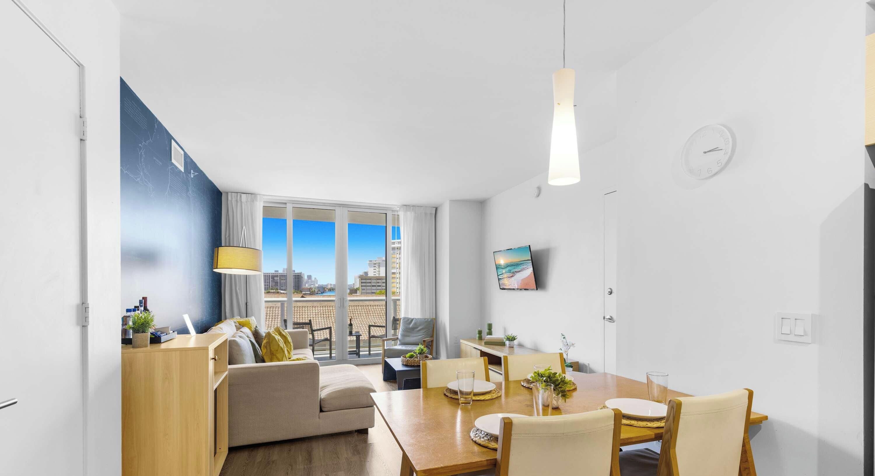 Een moderne woonkamer met een bank, een eettafel en stoelen, een groot raam met uitzicht op de stad, en een wandklok.