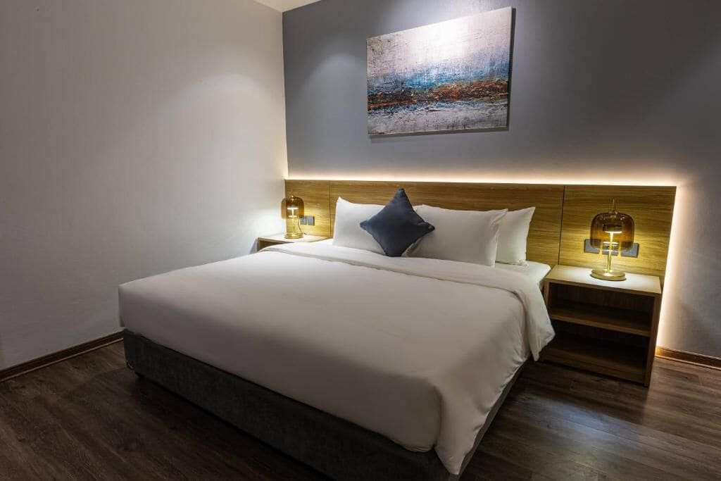 A hotel room with a large bed, two bedside tables with lamps, a painting on the wall, and wooden flooring.