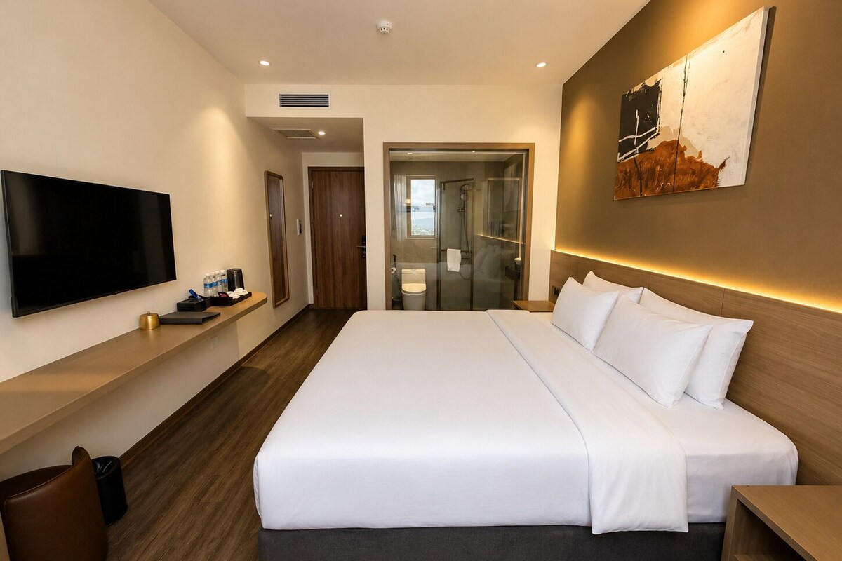 A modern hotel room with a large bed, a flat-screen TV, and a glass-enclosed shower area.