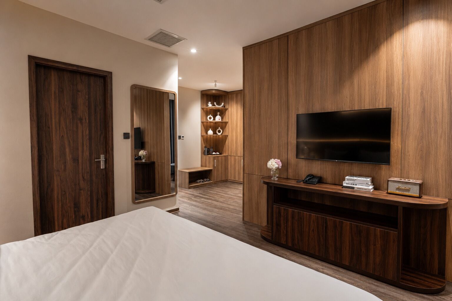 Una camera d'albergo con un letto, una televisione, un armadio in legno e un piccolo ripiano con degli oggetti.