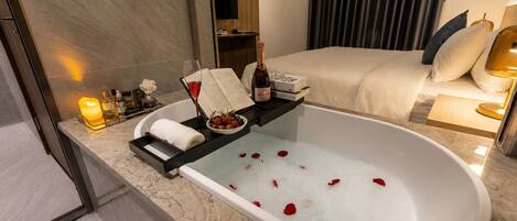 A modern bathroom with a bathtub, a vanity with toiletries, a bed, and a large mirror.