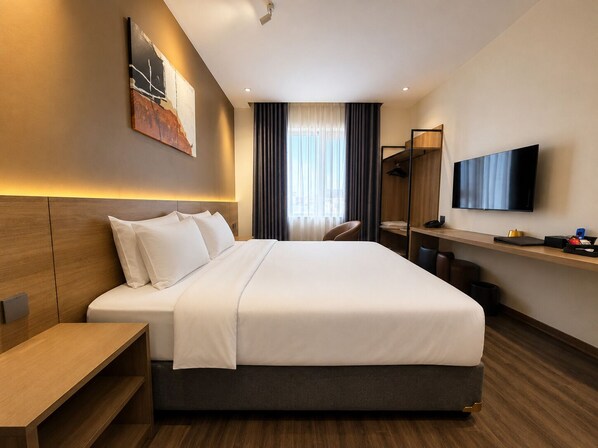 A modern hotel room with a large bed, bedside tables, a desk, a television, and a wardrobe.
