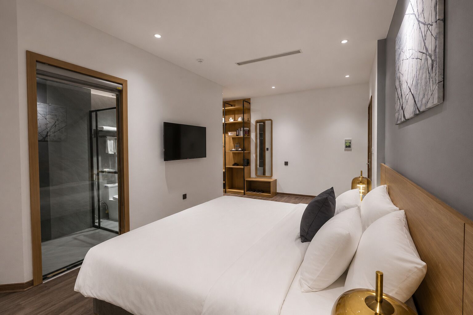 A modern hotel room with a large bed, a television, a wardrobe, and a glass shower enclosure.
