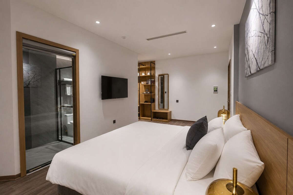 A modern hotel room with a large bed, a television, a wardrobe, and a glass shower enclosure.