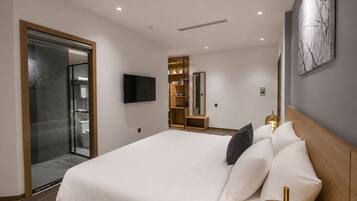 A modern hotel room with a large bed, a television, a wardrobe, and a glass shower enclosure.